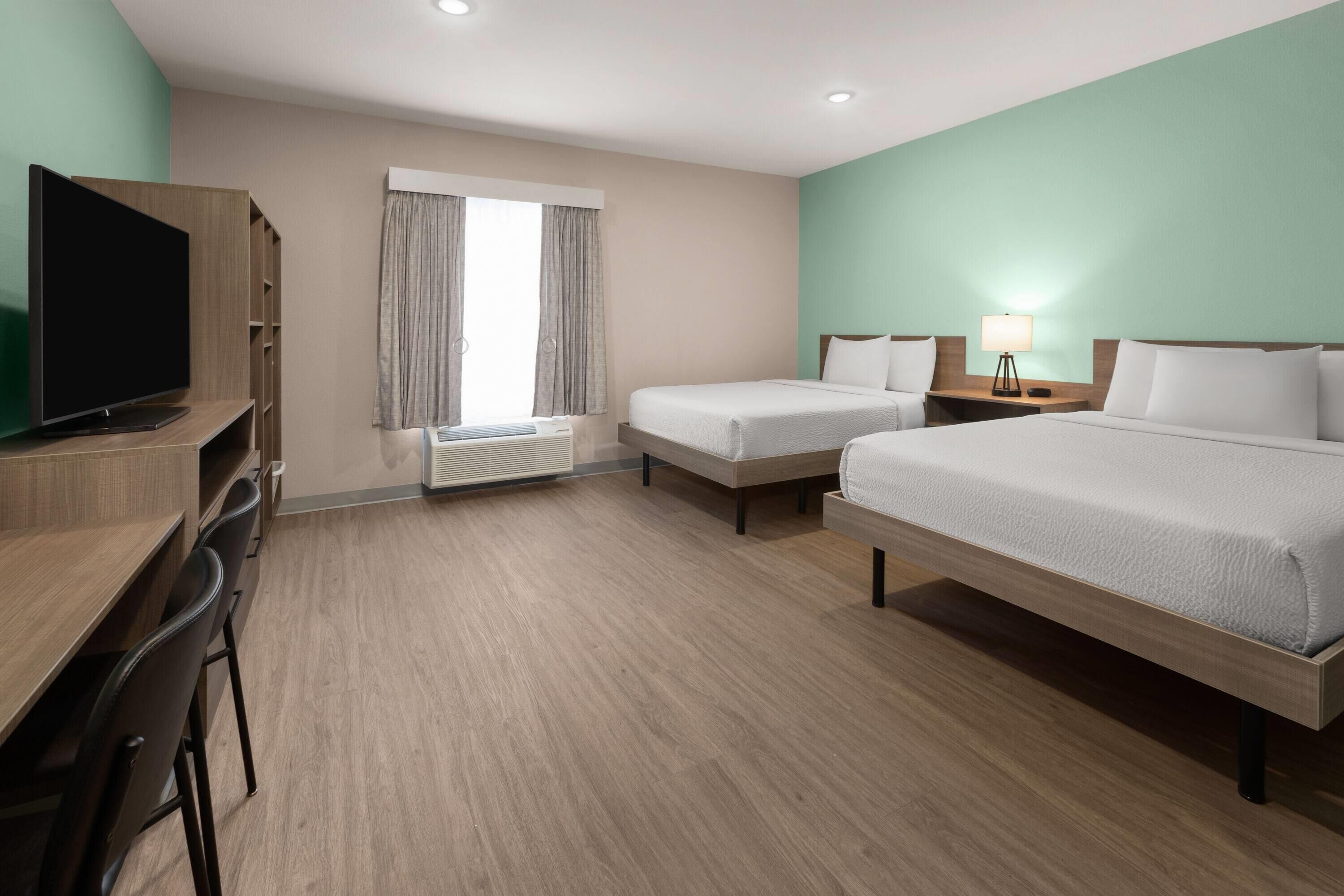 A hotel room with a bed, a desk, a TV, and a window with curtains.