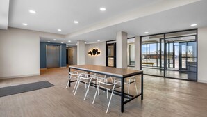 A spacious conference room with a long table and white chairs, a modern light fixture, and large glass doors leading to an outdoor area.