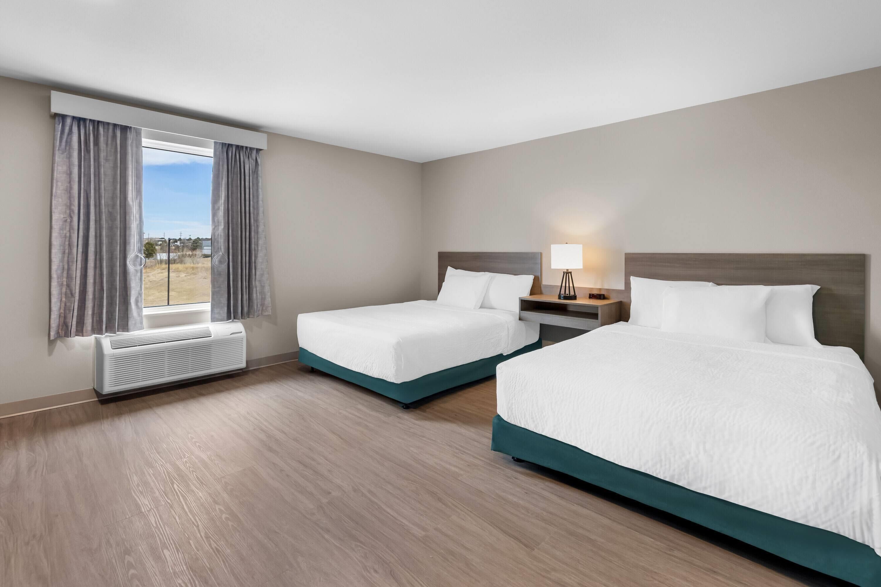 Une chambre d’hôtel avec deux lits, une fenêtre avec des rideaux, une table de chevet avec une lampe et un climatiseur fixé au mur.