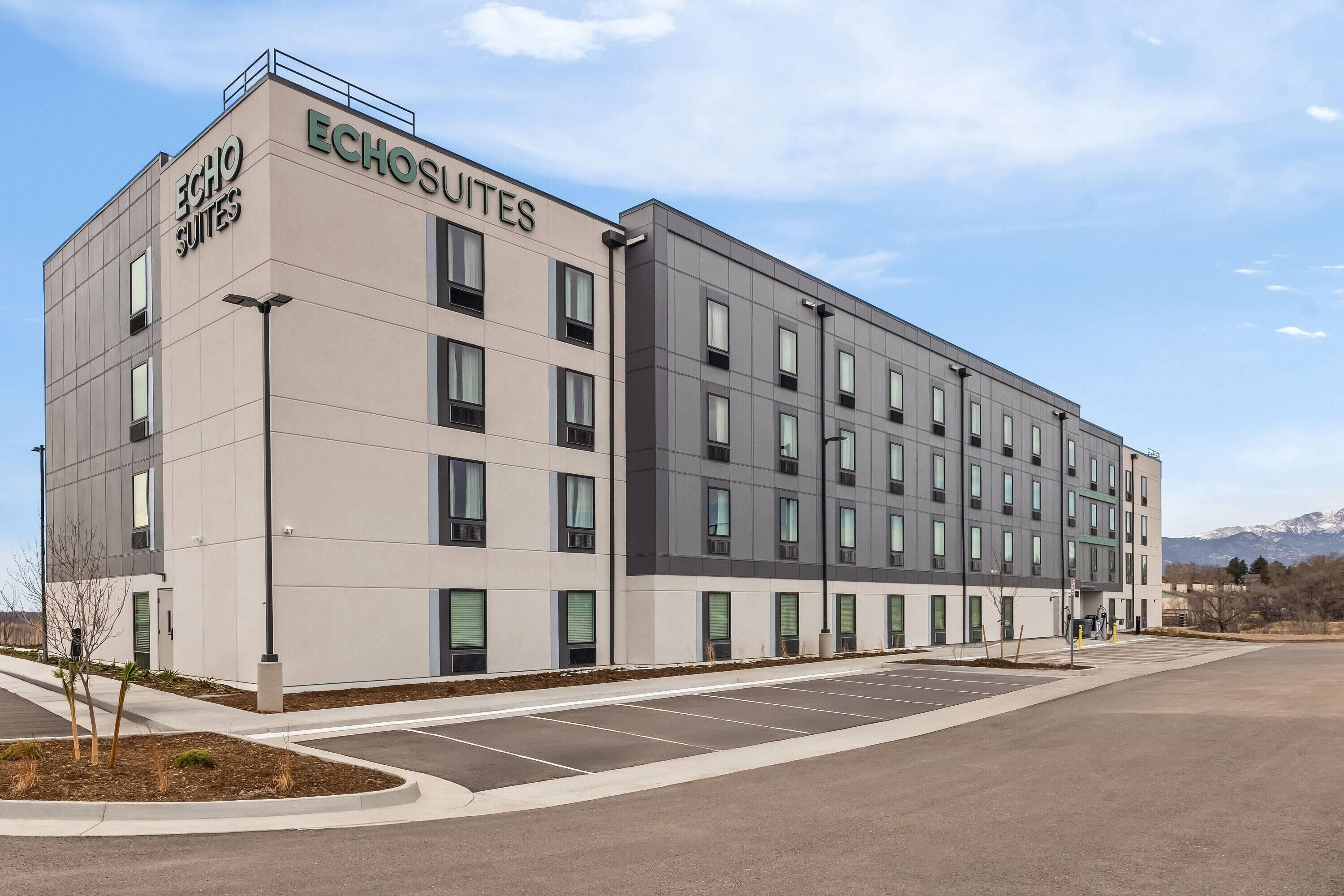 Un moderno edificio de hotel con la señalización 'Echo Suites', varios pisos y un estacionamiento.