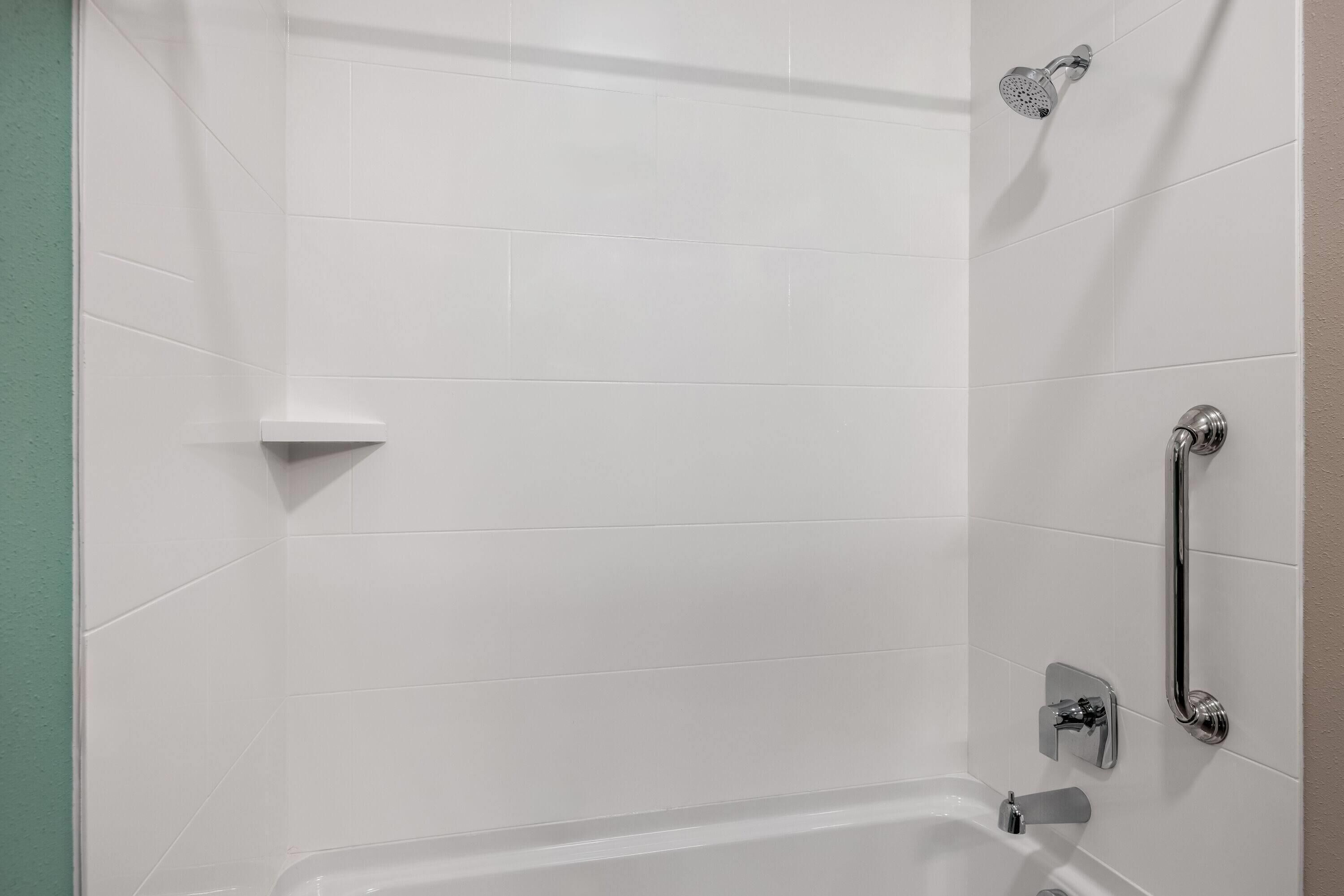 Ein Badezimmer mit weißen Fliesen, einer Badewanne, einer Duschbrause und einer Haltestange.