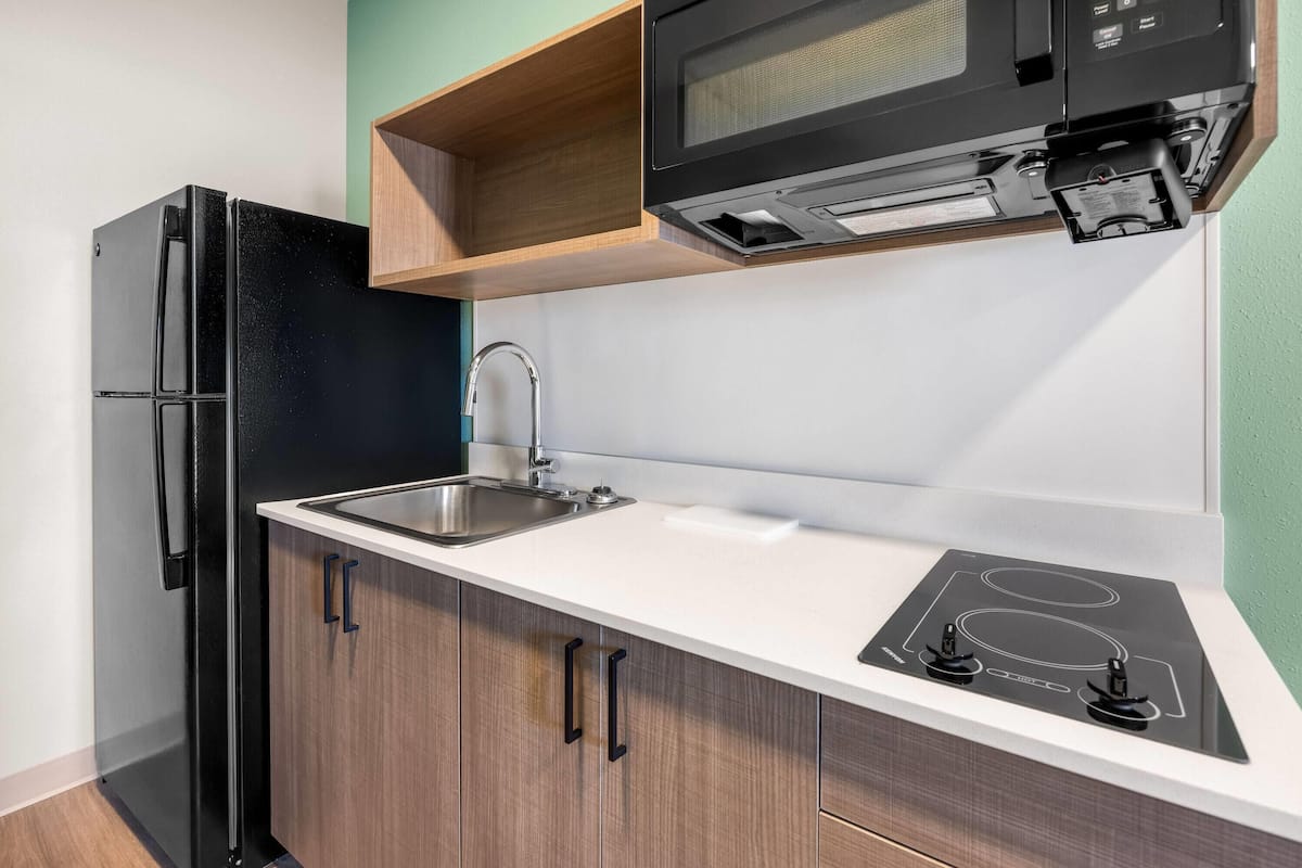 A compact kitchen with a black refrigerator, a built-in microwave, a sink, and a stovetop.