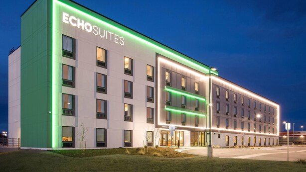 A modern hotel building with the name 'Echosuites' illuminated on the facade.