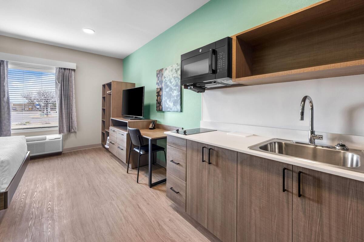 A modern kitchenette with a microwave, sink, and wooden cabinets.