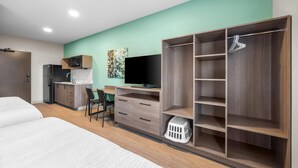 A modern hotel room with a bed, a desk, a television, a wardrobe, and a laundry basket.