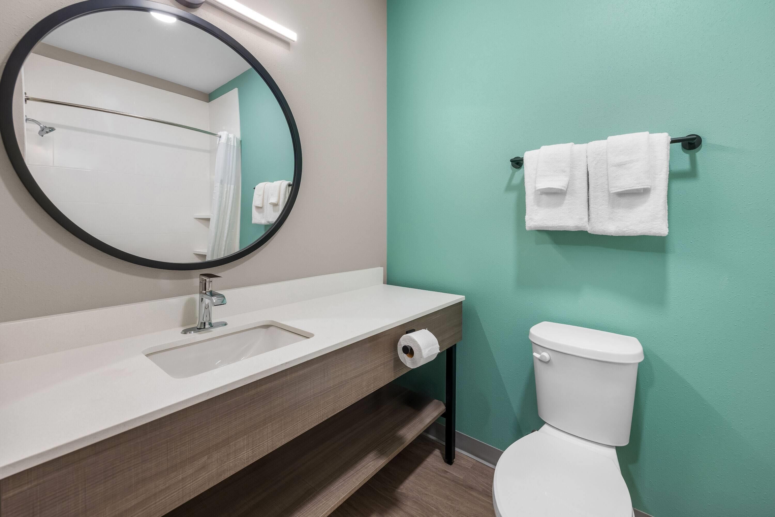 Ein Badezimmer mit rundem Spiegel, Waschbecken, Toilette und Handtuchhalter.
