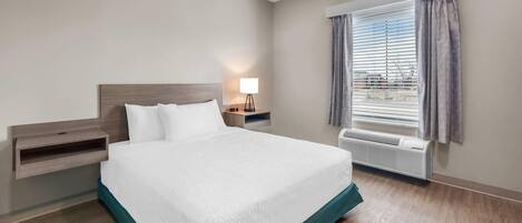 Une chambre d’hôtel équipée d’un lit, d’une table de chevet, d’une lampe, d’une fenêtre avec stores et d’un appareil de climatisation.