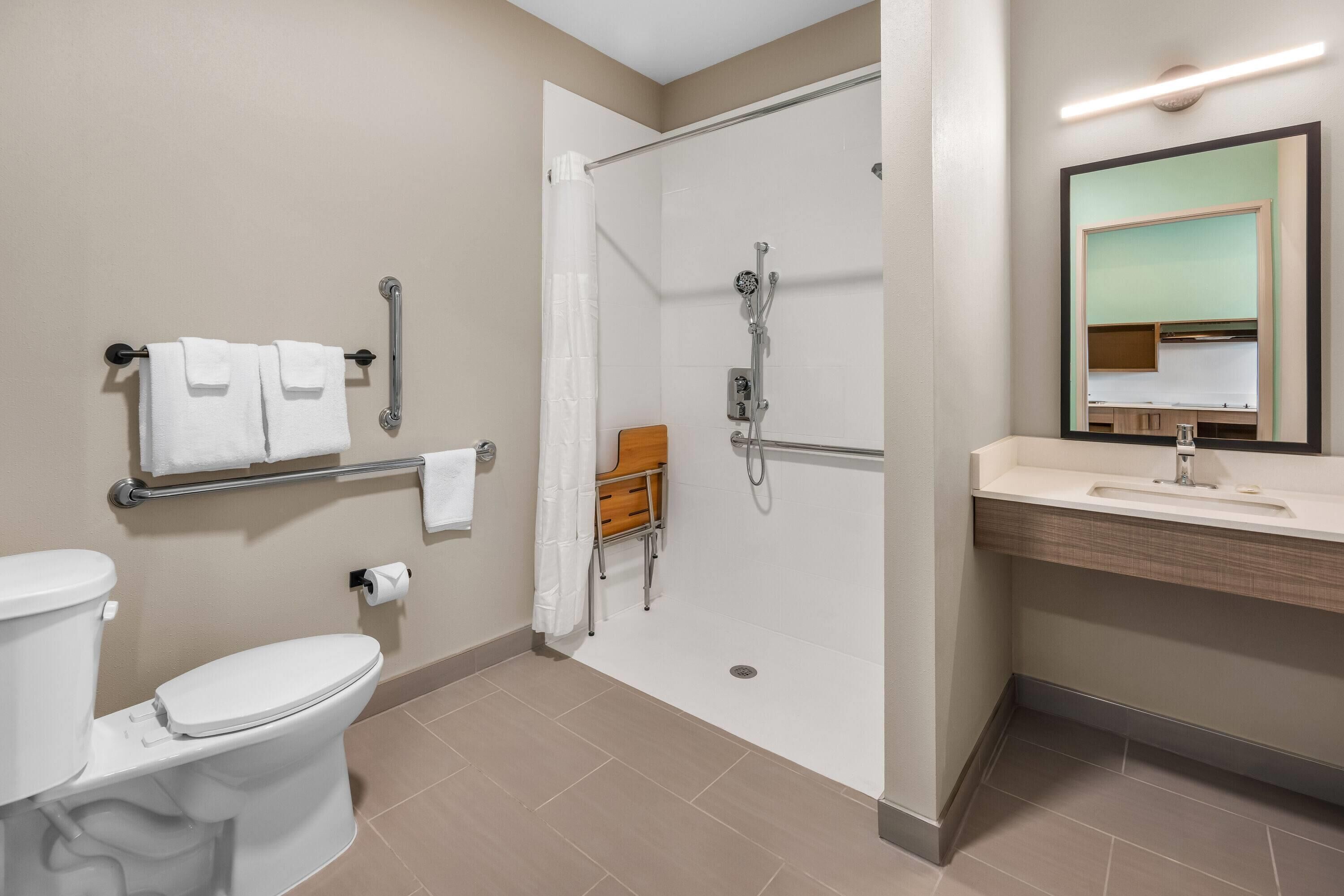 Ein Badezimmer mit Toilette, einer Dusche mit Glastür, einem Waschbecken mit Spiegel und einem Handtuchhalter.