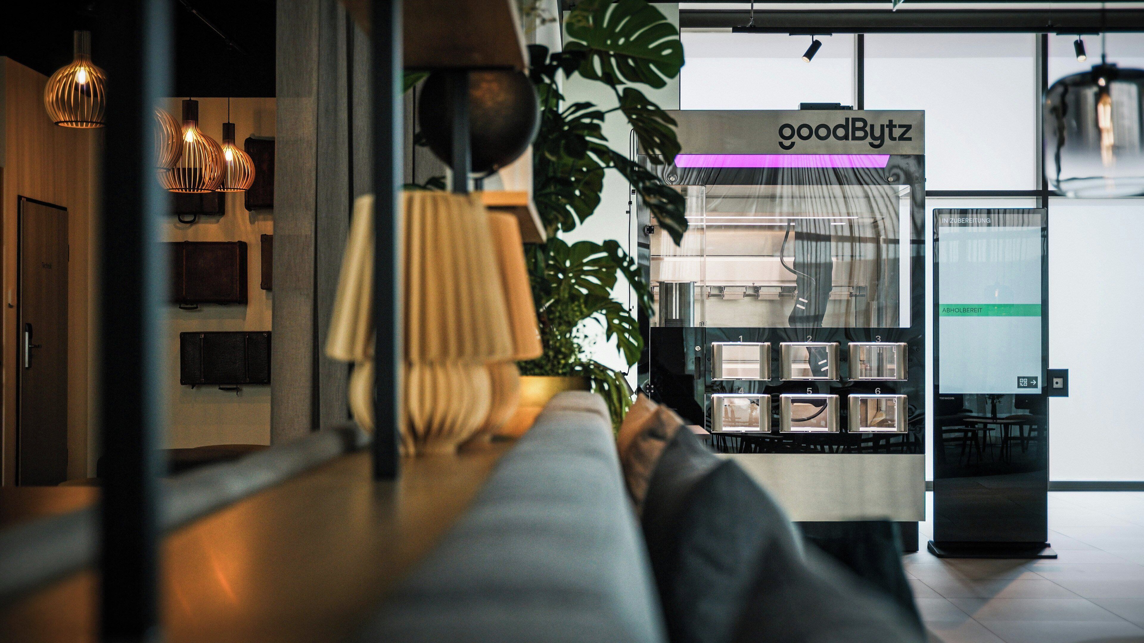 Ein modernes Interieur mit einer Sitzecke, einer Pflanze und einem Schild mit der Aufschrift 'goodBytz'.