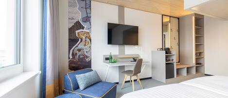 Quarto de hotel moderno com cama, escrivaninha, cadeira, televisão e guarda-roupa.