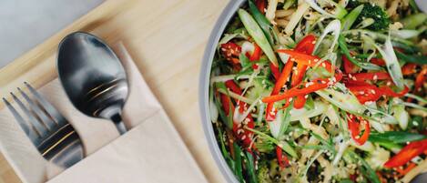 A bowl of salad with various vegetables and sesame seeds on a wooden tray.