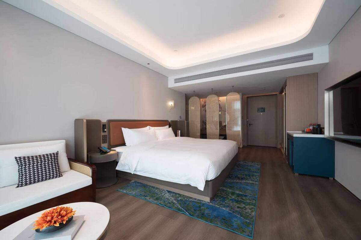 A modern hotel room with a large bed, a sofa, a desk, and a TV.