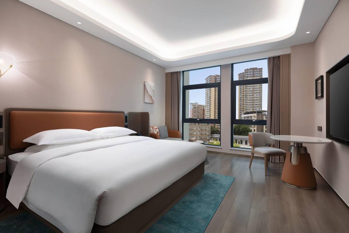 A modern hotel room with a large bed, a seating area, and a TV.