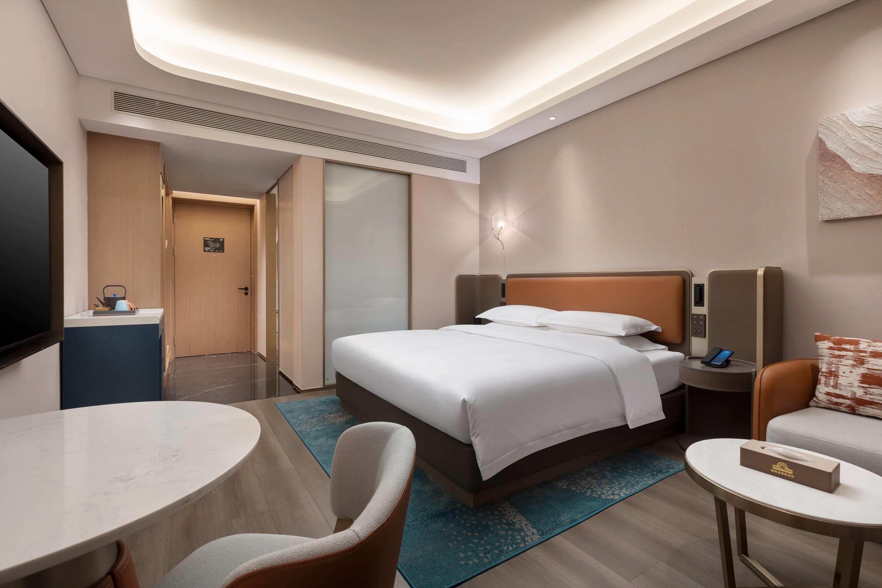 A hotel room with a bed, a desk, a chair, a TV, and a bedside table.