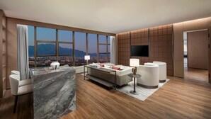 Una habitación de hotel moderna con un ventanal grande, un sofá, un televisor y una encimera de mármol.