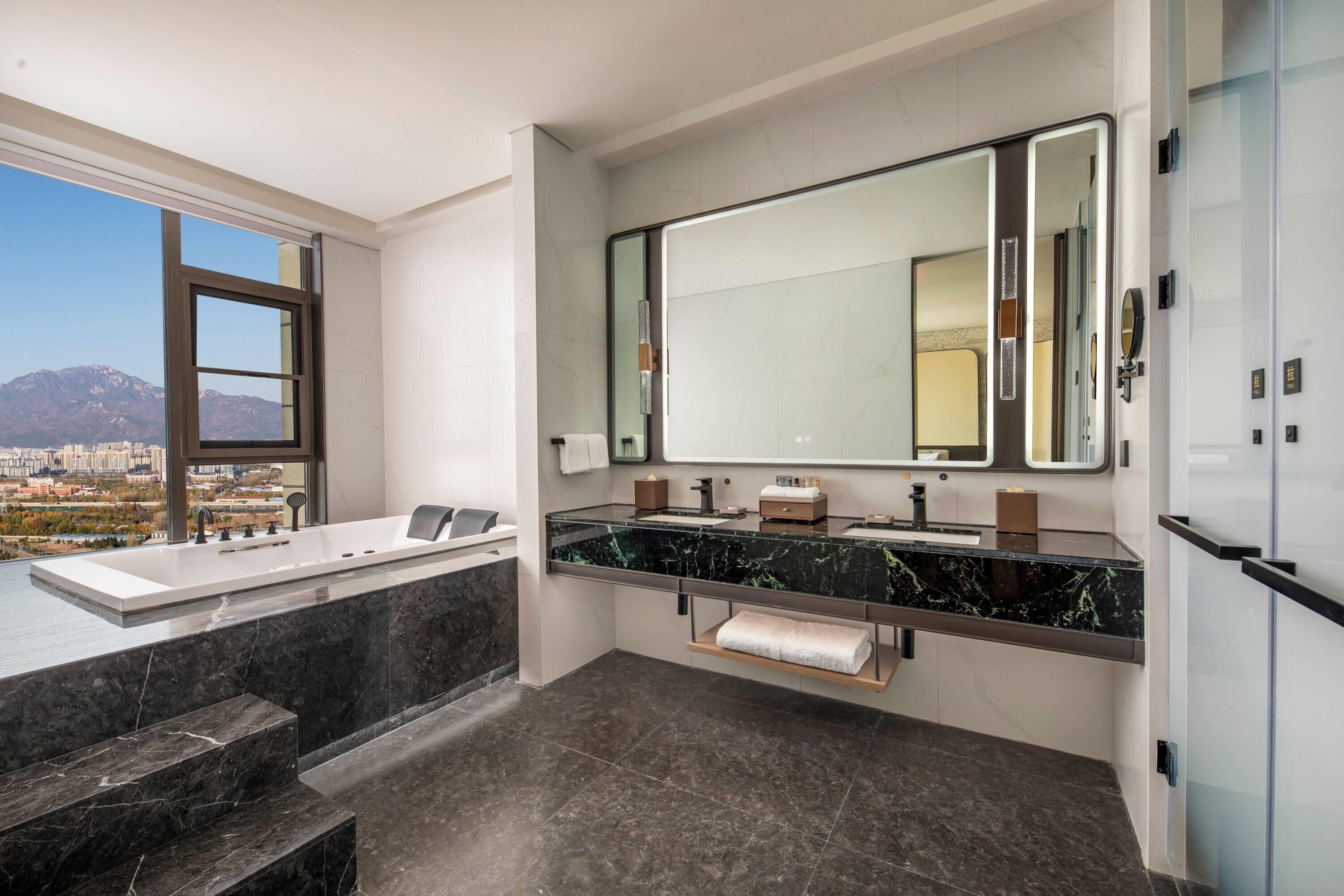 Une salle de bain moderne avec un grand miroir, une baignoire et un meuble-lavabo doté d’un plan de travail en marbre.