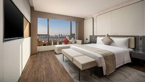 Una habitación de hotel moderna con una cama grande, una zona de estar y vistas a la ciudad.