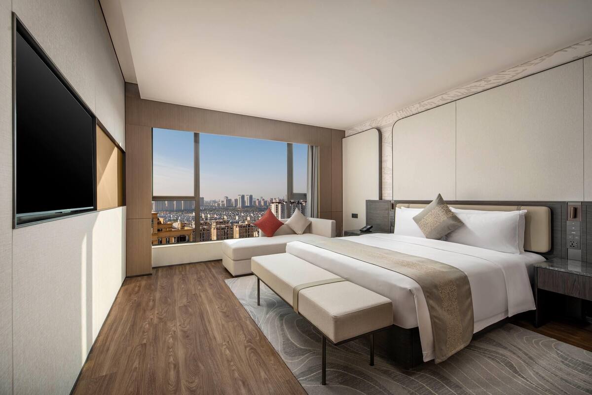 A modern hotel room with a large bed, a seating area, and a city view.