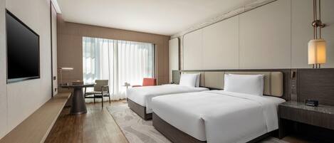 Habitación de hotel moderna con dos camas, un televisor de pantalla plana, un escritorio y un ventanal con cortinas translúcidas.