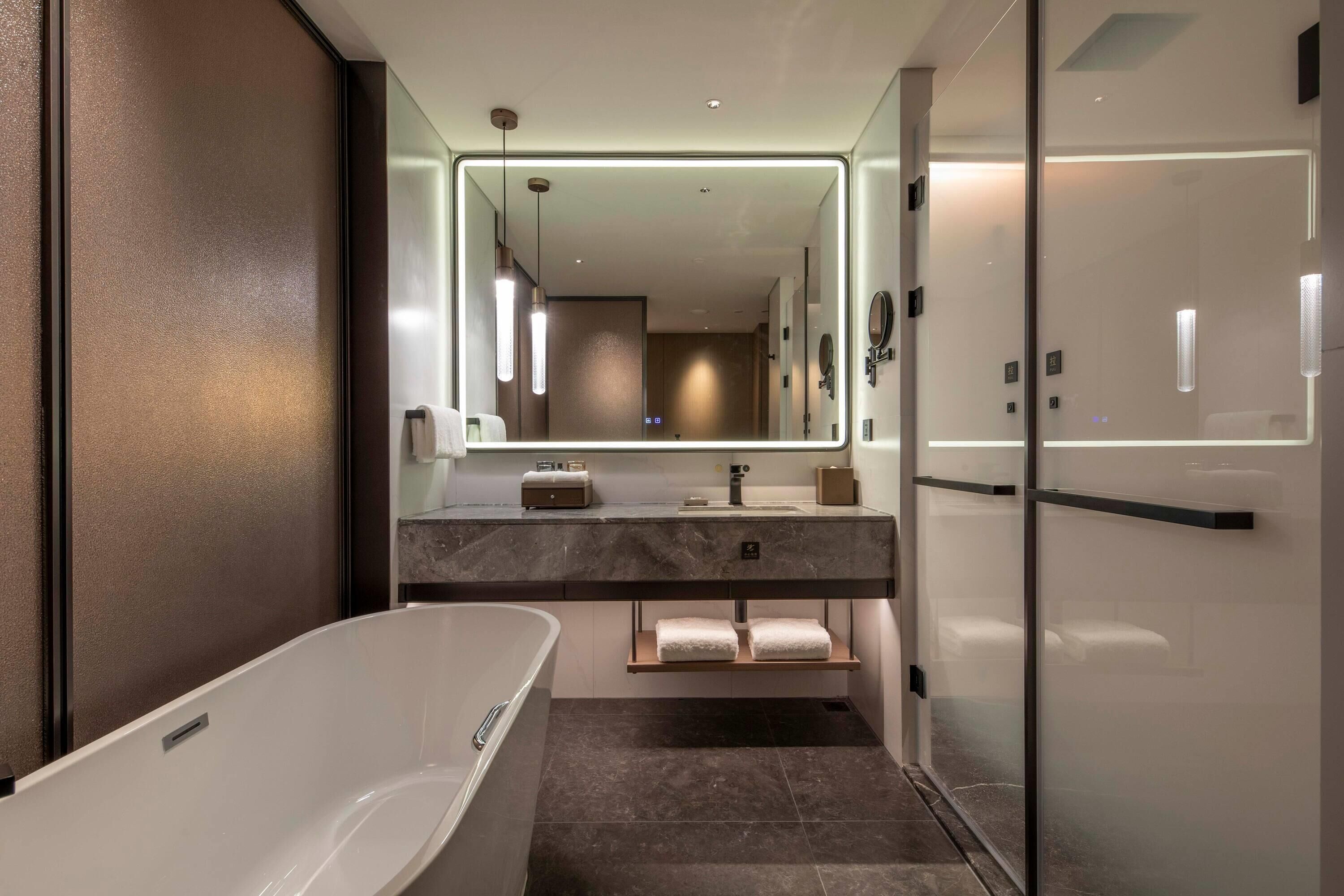 A modern bathroom with a freestanding bathtub, a large mirror, and a vanity with a marble countertop.