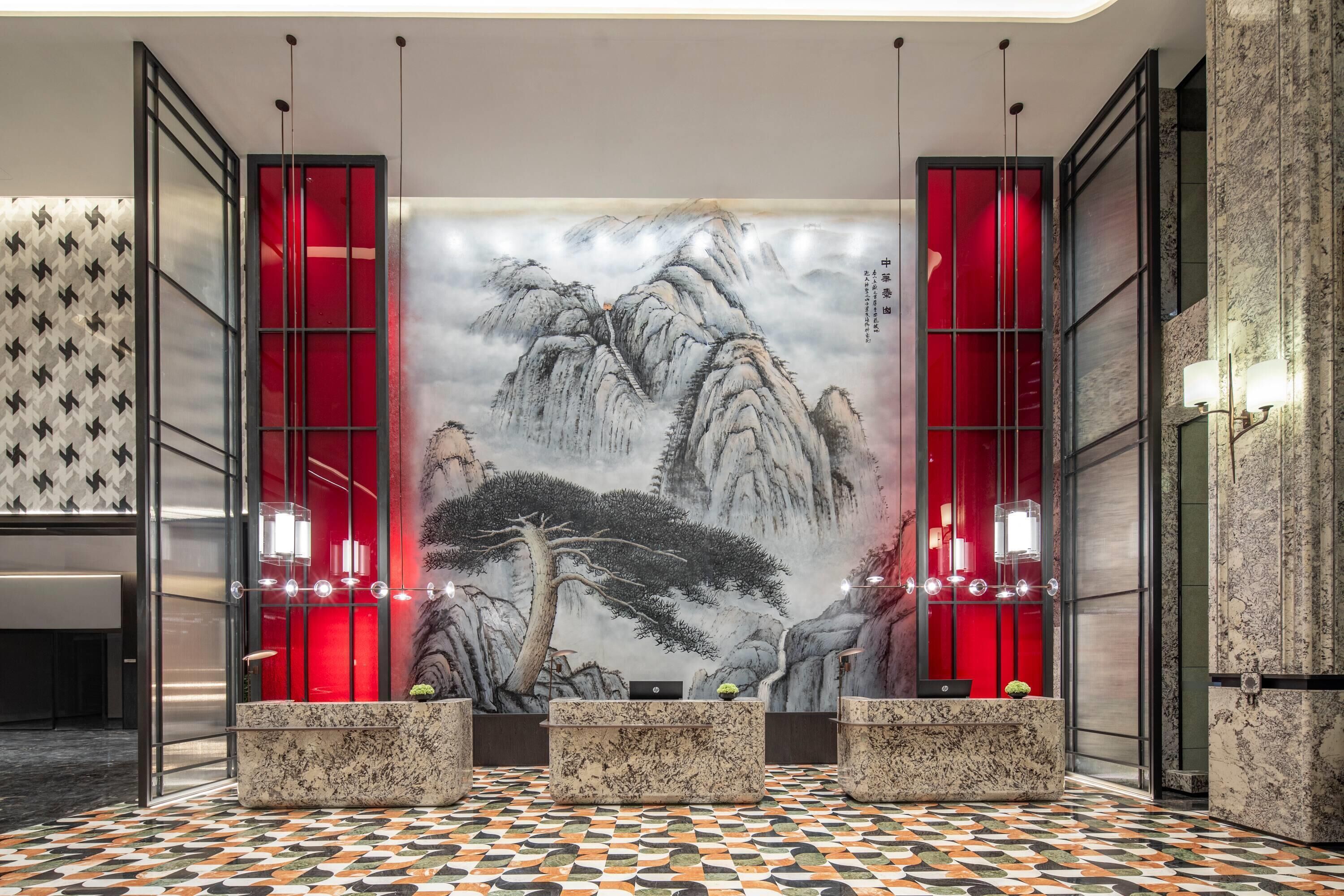 A lobby with a traditional Chinese landscape painting, red accents, and a modern design.