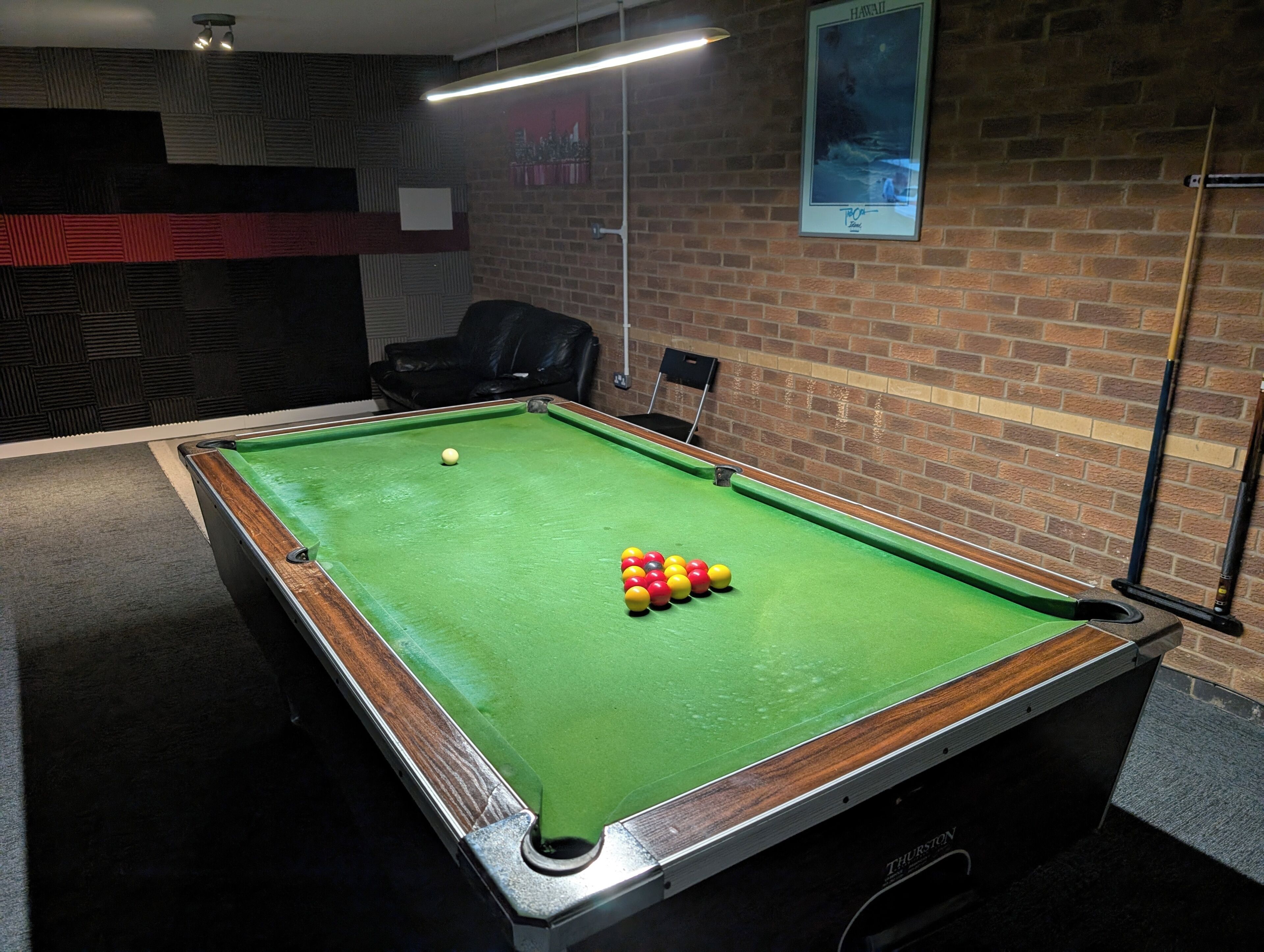 A pool table with balls, a chair, and a poster on a brick wall.
