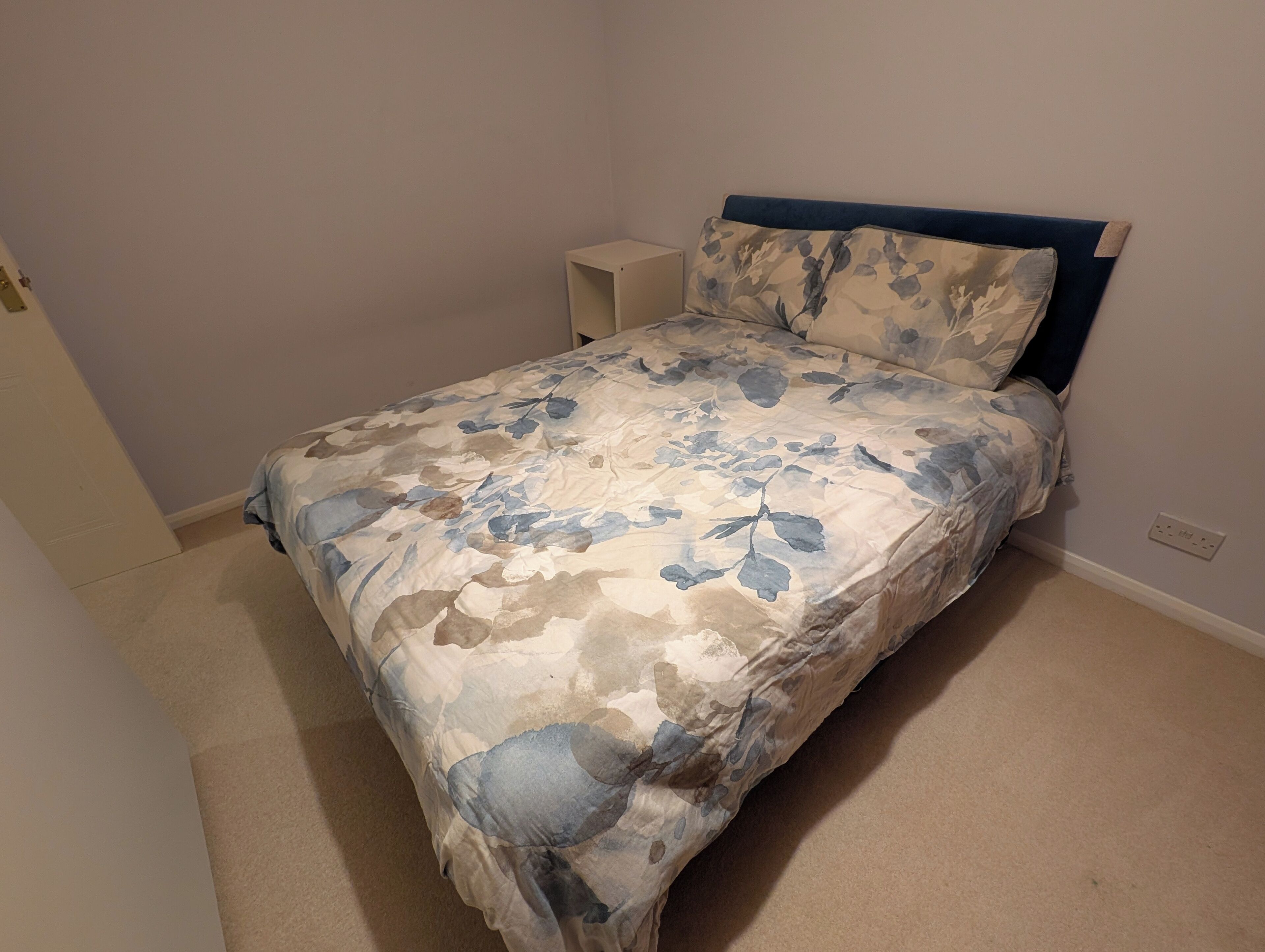 A bedroom with a bed, a nightstand, and a wall socket.