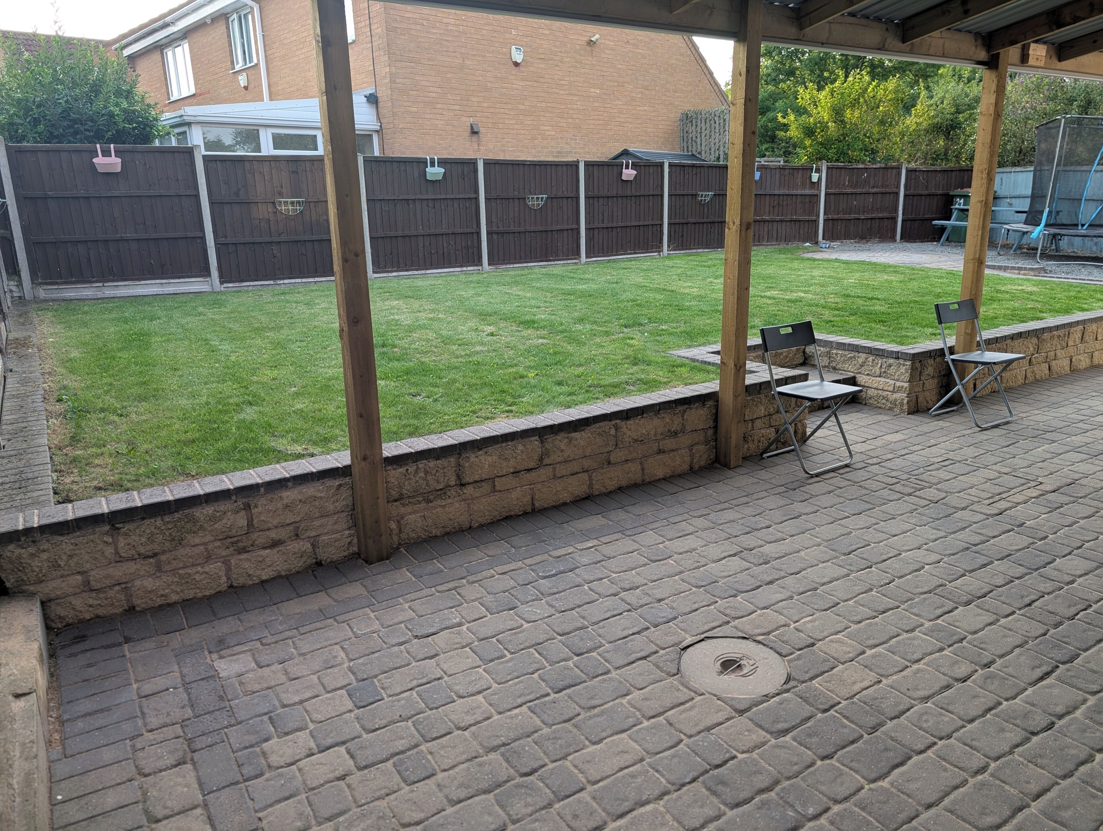 A backyard with a brick patio, a wooden fence, and a grassy lawn.