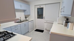 A compact kitchen with light blue cabinets, a white countertop, a built-in stove, a dishwasher, and a window. - Spacious 3 bedroom Family house with games room in quiet area (Braunstone Town)