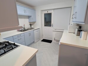 Una cocina compacta con gabinetes azul claro, encimera blanca, horno empotrado, lavavajillas y una ventana.