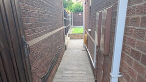 A narrow brick pathway leading to a gated area with a grassy yard visible in the distance. - Spacious 3 bedroom Family house with games room in quiet area (Braunstone Town)