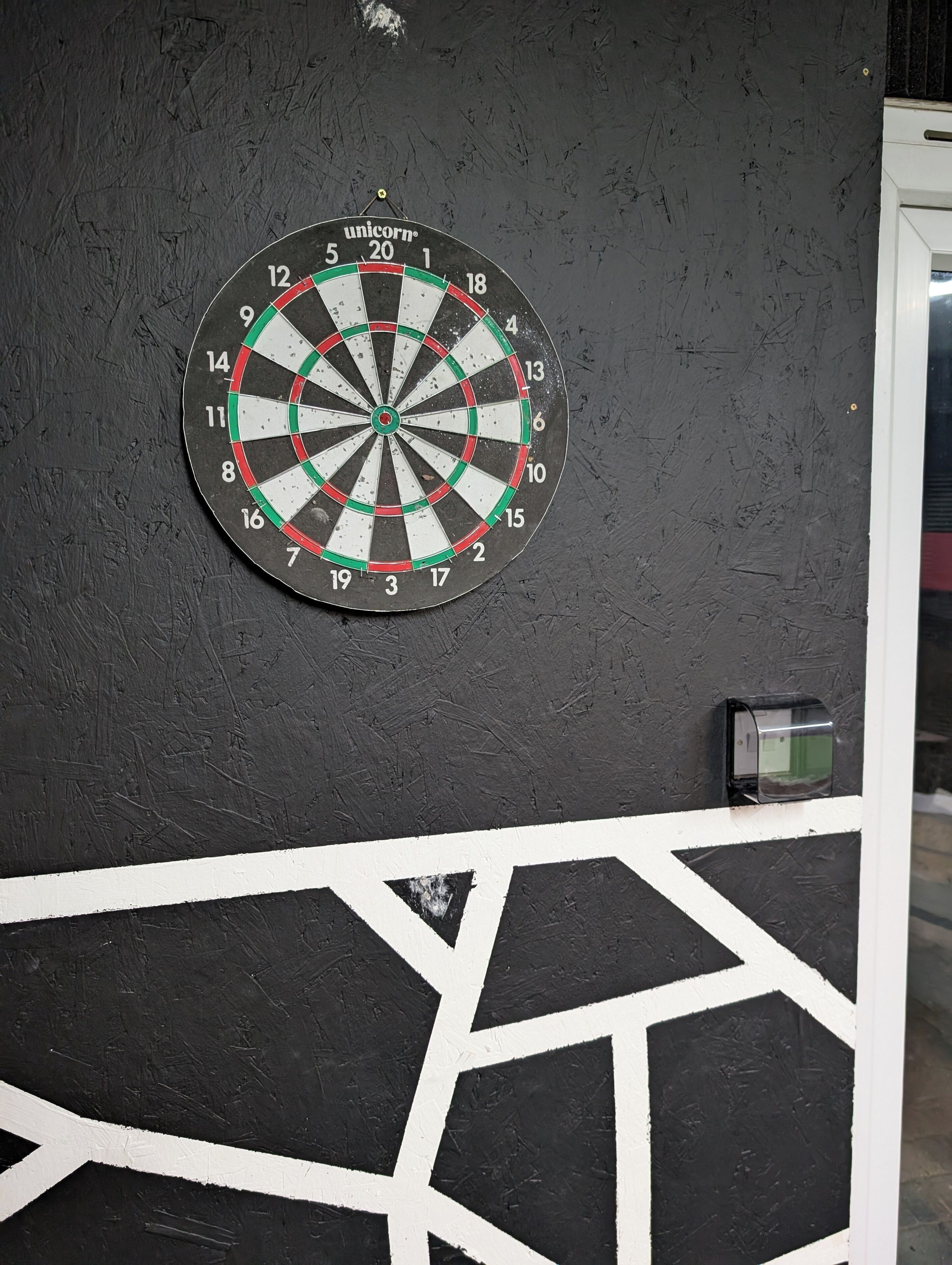 Eine Dartscheibe an einer Wand mit strukturierter Oberfläche und einem geometrischen Muster darunter.