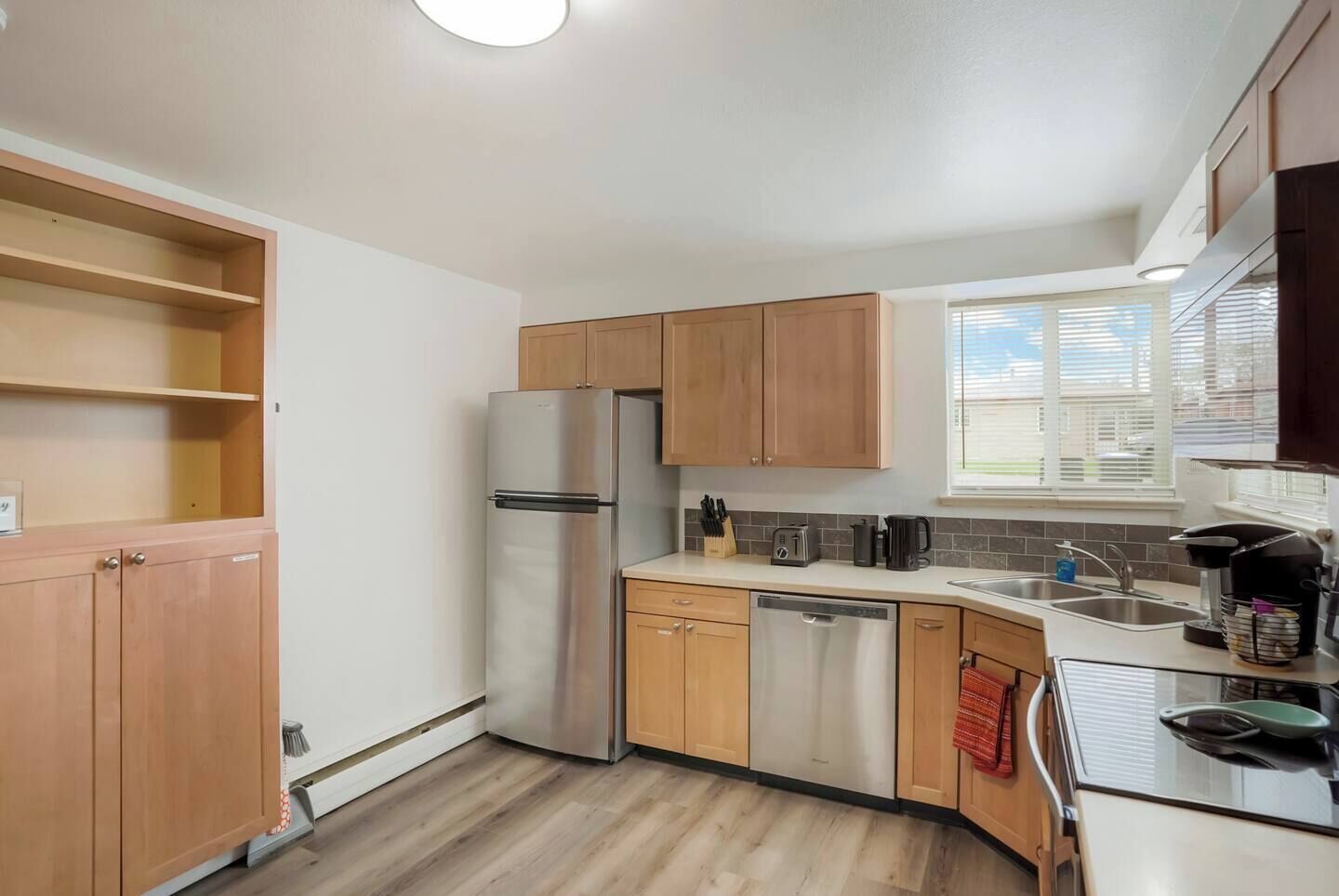 Cocina compacta con armarios de madera, un refrigerador de acero inoxidable, lavavajillas y una ventana que proporciona luz natural.