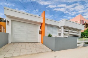 Ein modernes Haus mit Garage, einer hohen, orangefarbenen Säule und einem grauen Zaun.