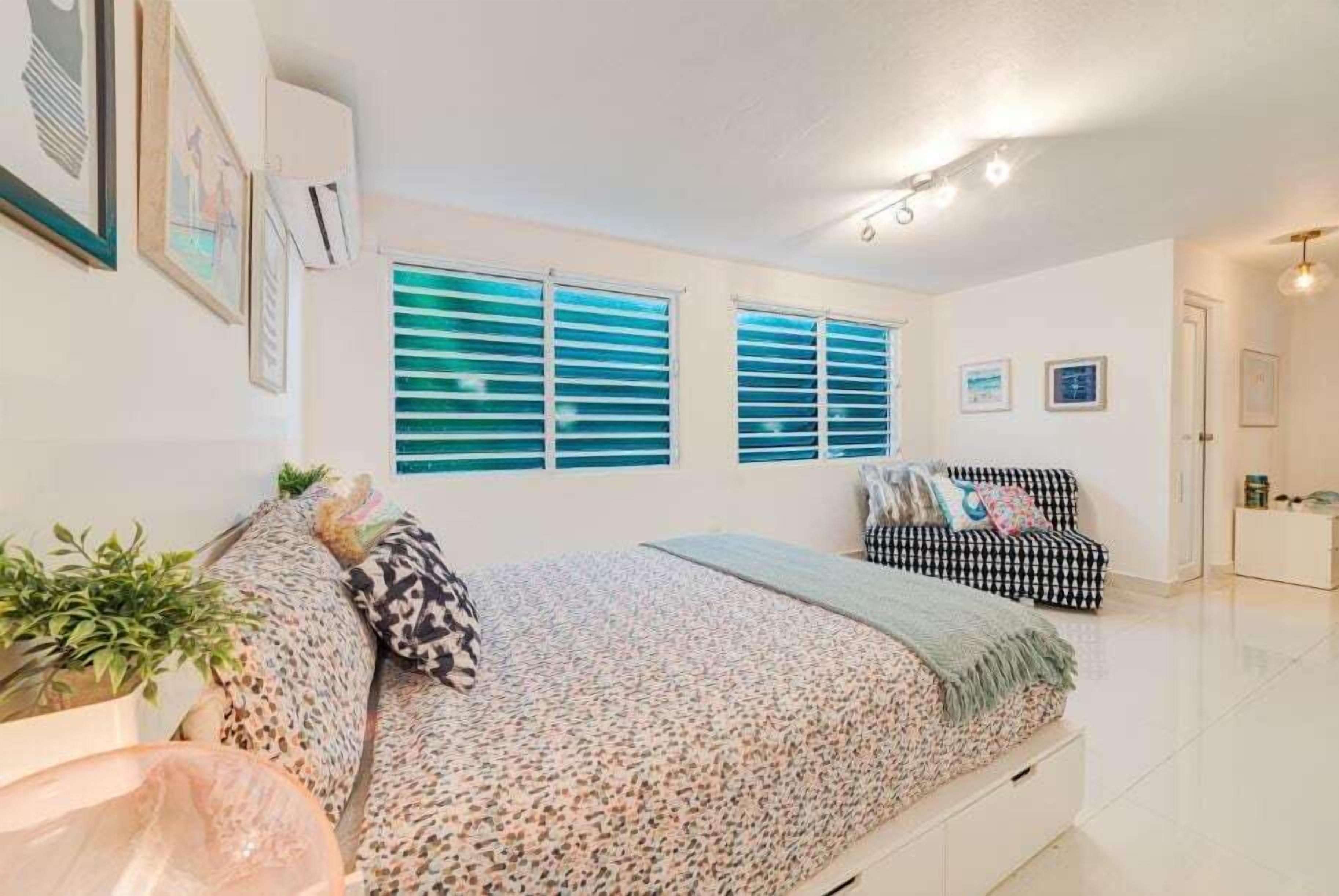 A bedroom with a bed, a sofa, and a window with blinds.