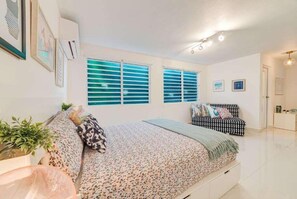 A bedroom with a bed, a sofa, and a window with blinds. - Casa Monsita: Colorful Vibes by the Beach (Monsita)