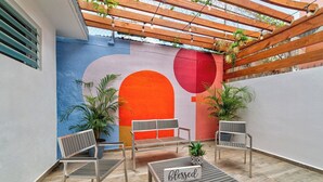 Un espace extérieur aménagé avec une pergola en bois, un banc et une table sur laquelle est posé un panneau.