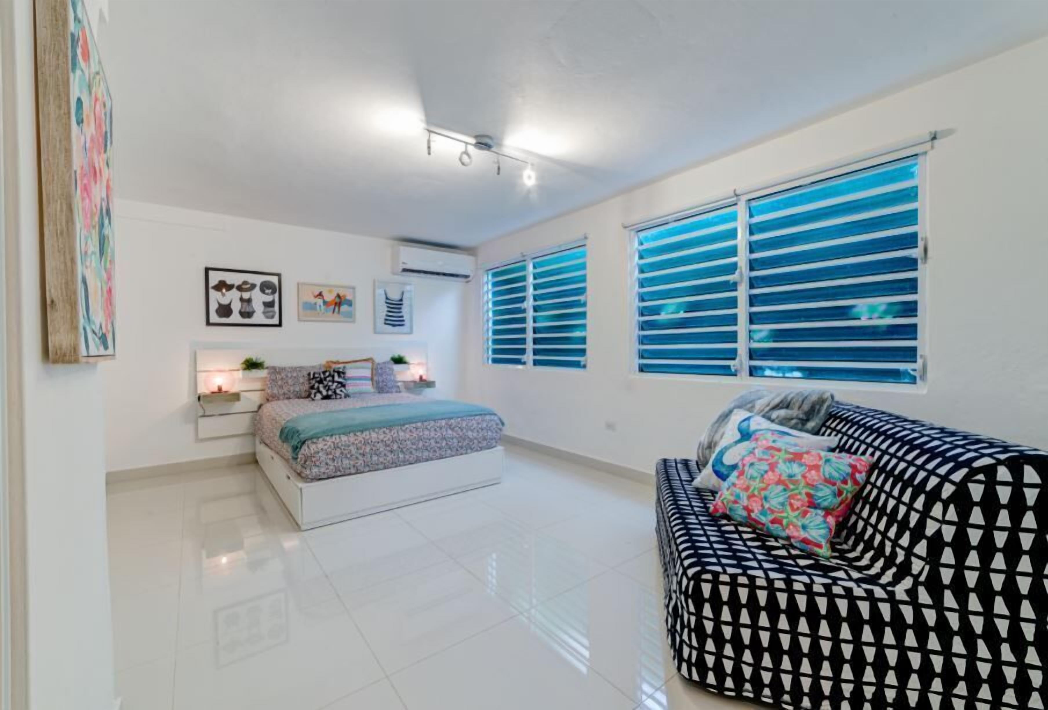 Une chambre à coucher moderne avec un lit, un canapé et une fenêtre équipée de stores.