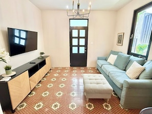Sala de estar con televisor de pantalla plana, un sofá, una mesa de centro y suelo estampado.