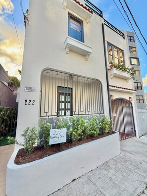 A modern building with a white facade, numbered 222, featuring a gated entrance and a small garden area. - Casa Santurce: Boho-chic home with Rooftop Oasis (Rosario)