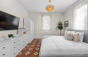 A bedroom with a bed, a TV, a dresser, a plant, and a window. - Casa Santurce: Boho-chic home with Rooftop Oasis (Rosario)