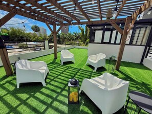 An outdoor seating area with white chairs and a table, surrounded by a wooden pergola and artificial grass. - Casa Santurce: Boho-chic home with Rooftop Oasis (Rosario)