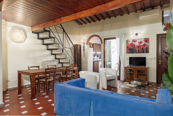 Un salon avec un escalier en bois, un coin repas, un canapé, une télévision et une grande plante.