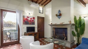 A living room with a fireplace, white chairs, a blue sofa, a glass coffee table, and a balcony with a chair and table. - Florence Slow-Life Flat in Oltrarno (Firenze)