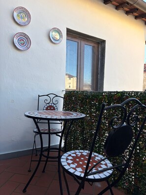 Une petite terrasse extérieure avec une table ronde et deux chaises, une fenêtre et des assiettes décoratives accrochées au mur.