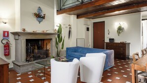 A living room with a fireplace, a blue sofa, white armchairs, a wooden dining table, and a tiled floor. - Florence Slow-Life Flat in Oltrarno (Firenze)