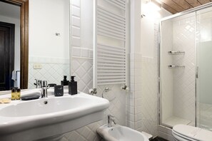 Une salle de bain avec un grand lavabo blanc, un bidet, une douche à parois de verre et un miroir.