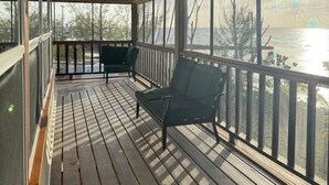 Eine überdachte Veranda mit Holzboden und Metallgeländern, mit zwei grünen Stühlen und Blick auf ein Gewässer.