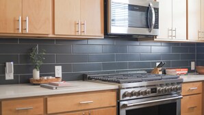 A modern kitchen with wooden cabinets, a stainless steel microwave, a gas stove, and a black tiled backsplash. - 3BR Downtown SA Home w/ Garage, Walk to Alamodome (San Antonio)
