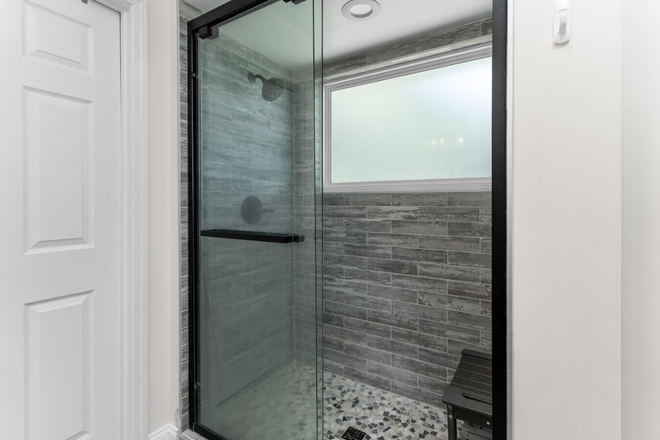 A glass-enclosed shower with a tiled wall and a bench.